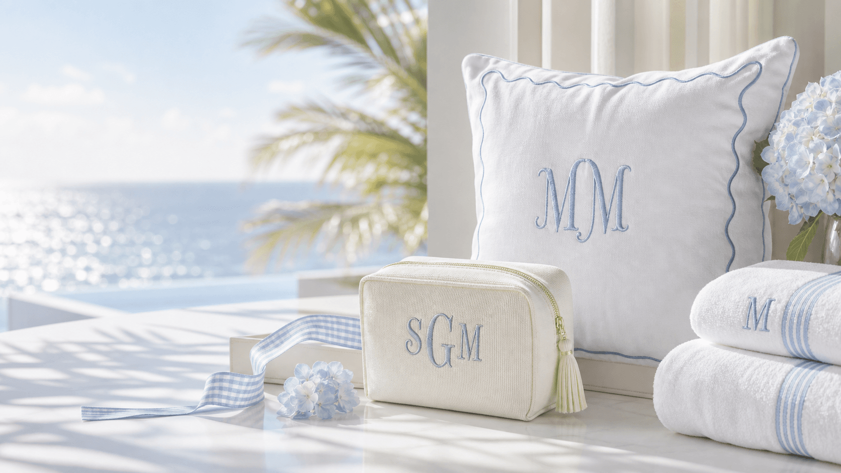 White pillow, ivory pouch, and folded towels with embroidered monograms in bright Miami coastal light